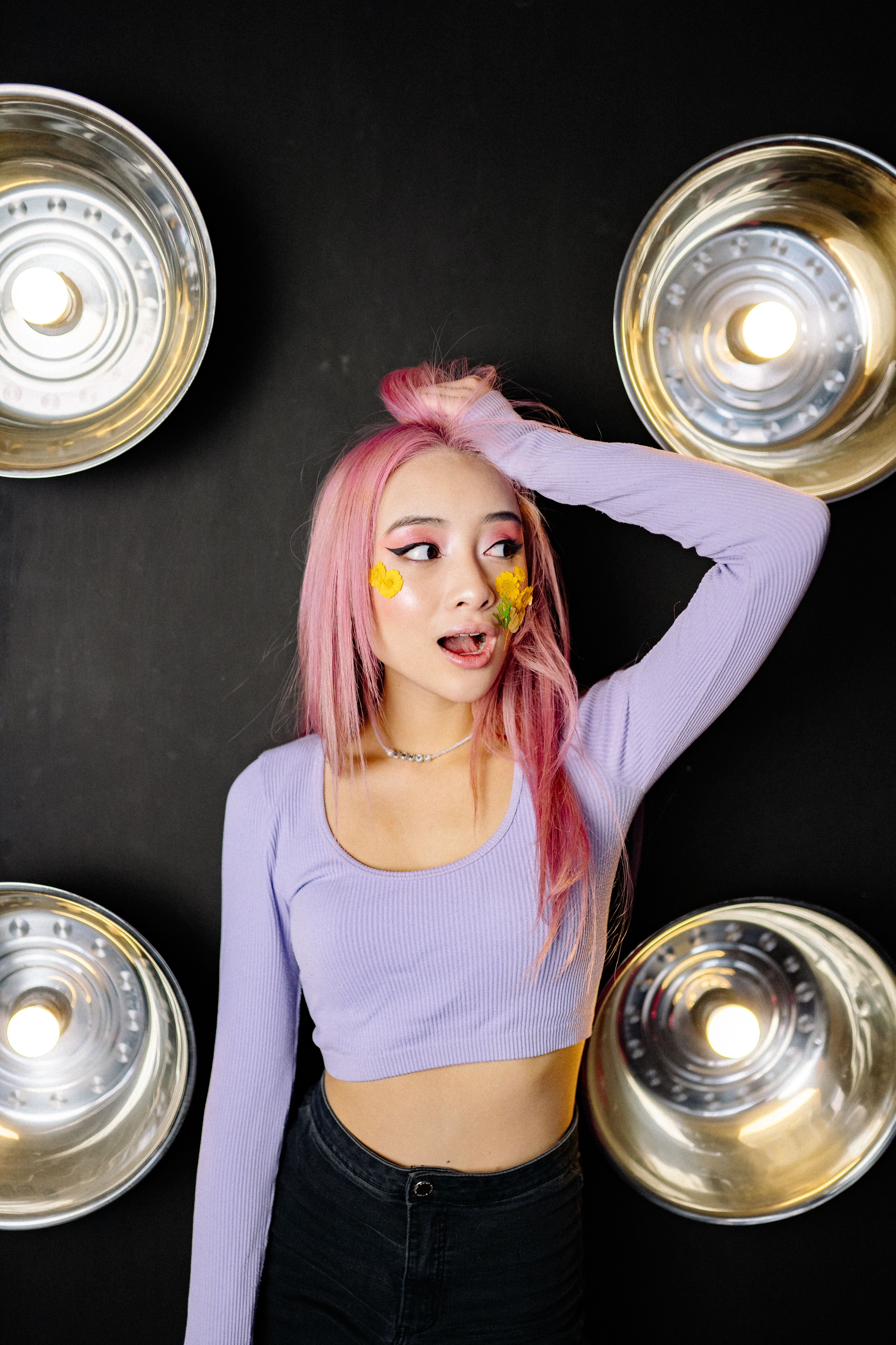 A young woman with pink hair, floral face art, and studio lighting for a creative photoshoot.