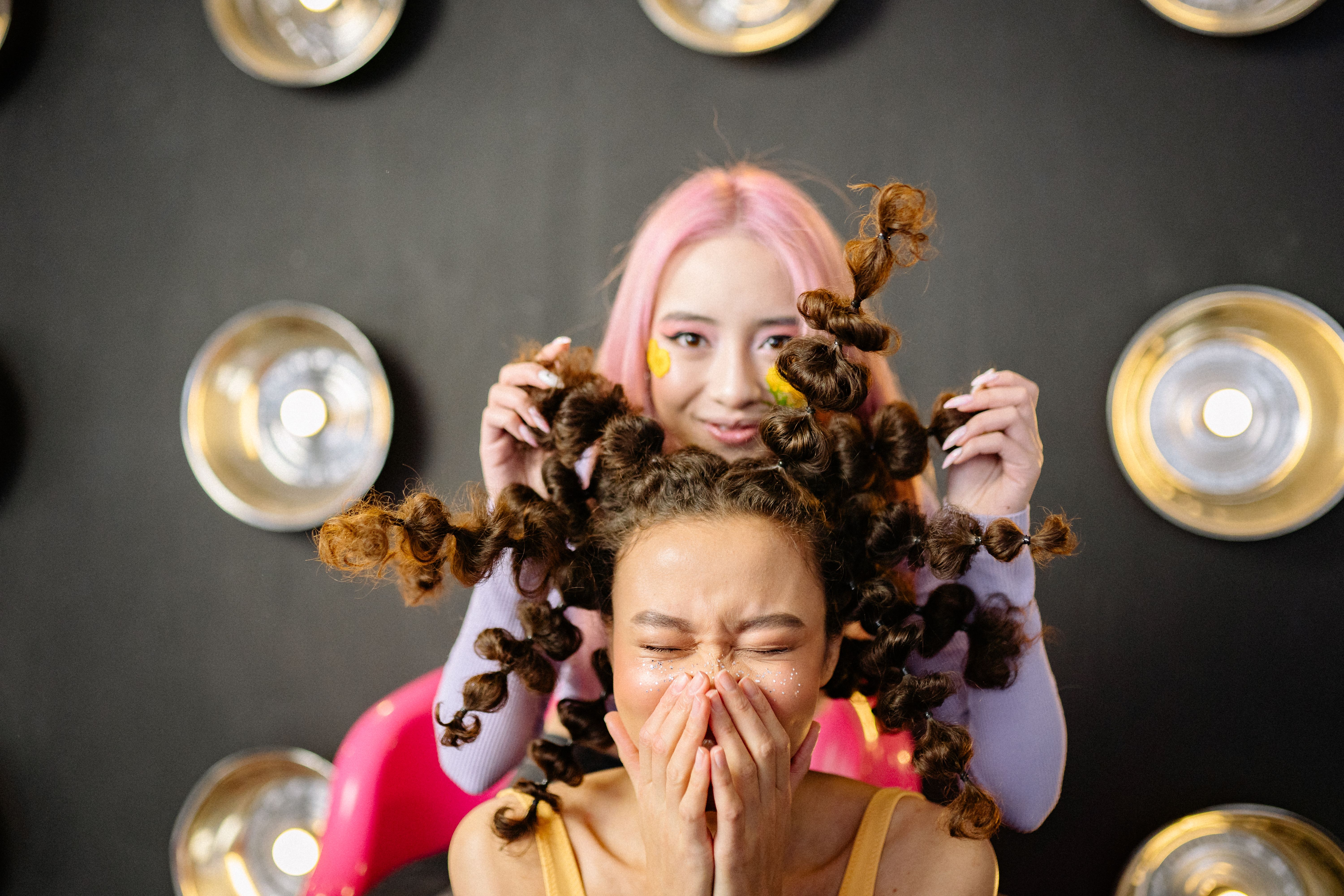 Two young women with creative hairstyles having fun in a stylish studio setting.