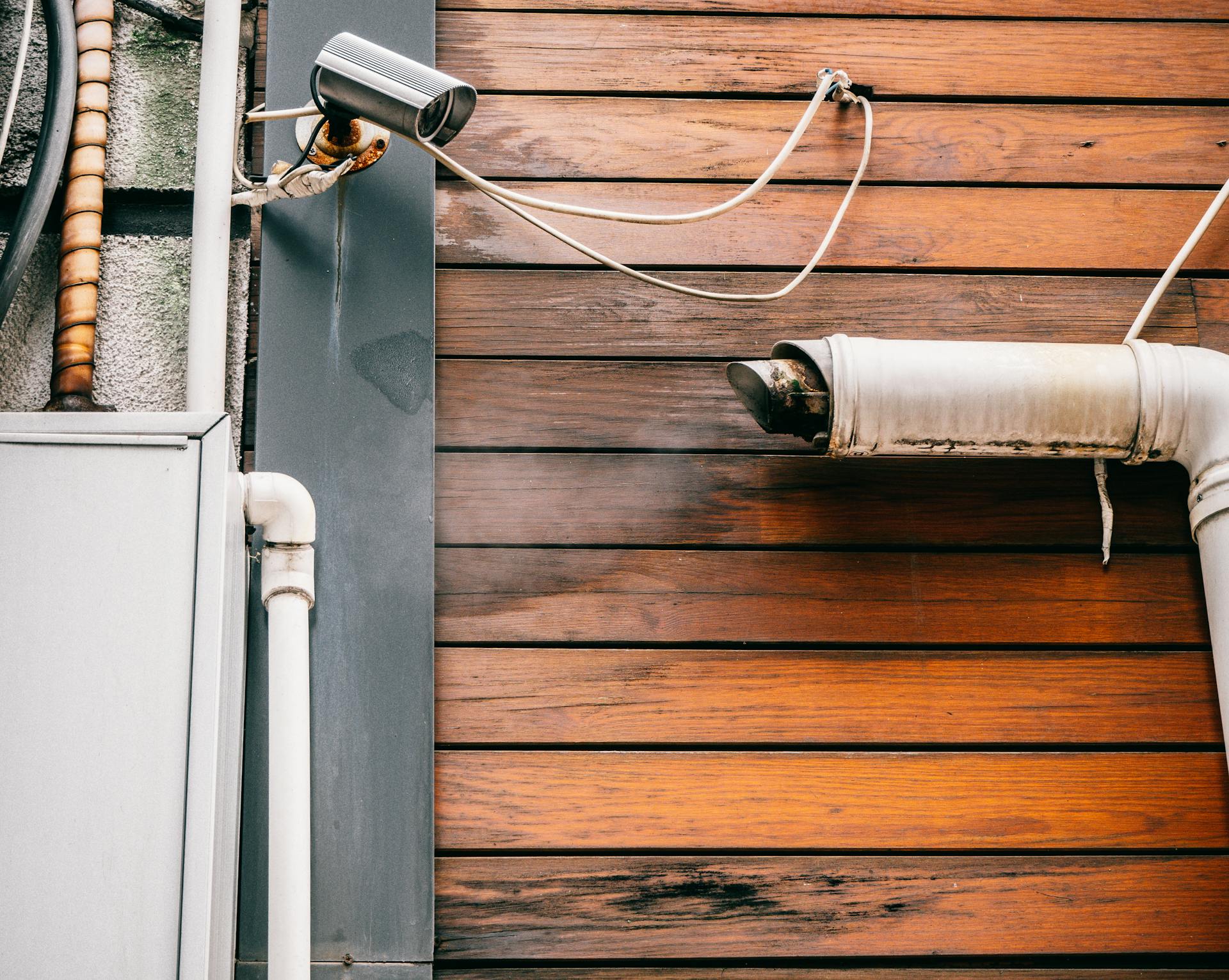 A detailed view of a rustic wooden wall featuring security camera and pipes, capturing urban architecture.