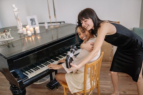 Free Two women joyfully embracing while capturing a moment by the piano, showcasing friendship and happiness. Stock Photo