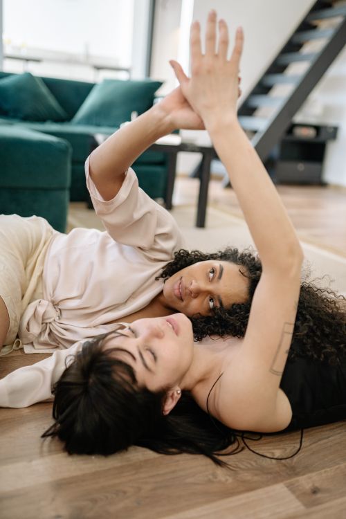 Free Two women lying on a floor, lovingly holding hands, enjoying each other's company indoors. Stock Photo