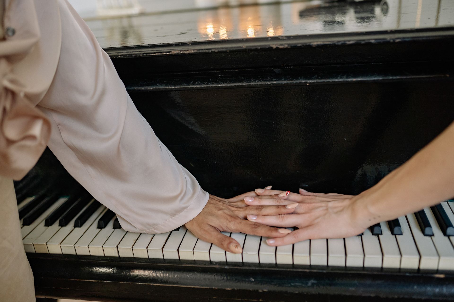 Two hands touching on a grand piano keyboard in a serene indoor setting.