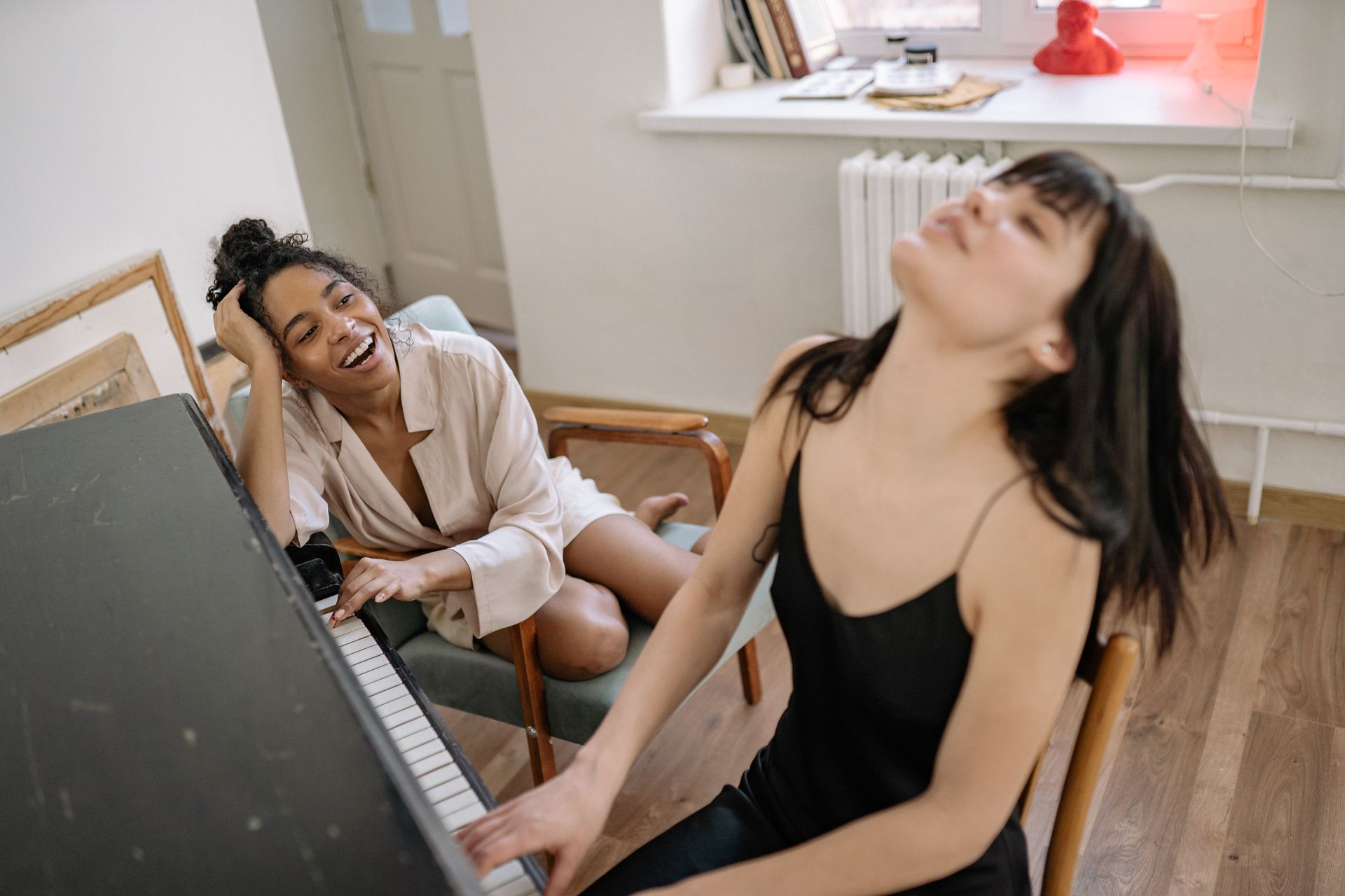 Two women smiling and enjoying a musical moment together while playing piano indoors.