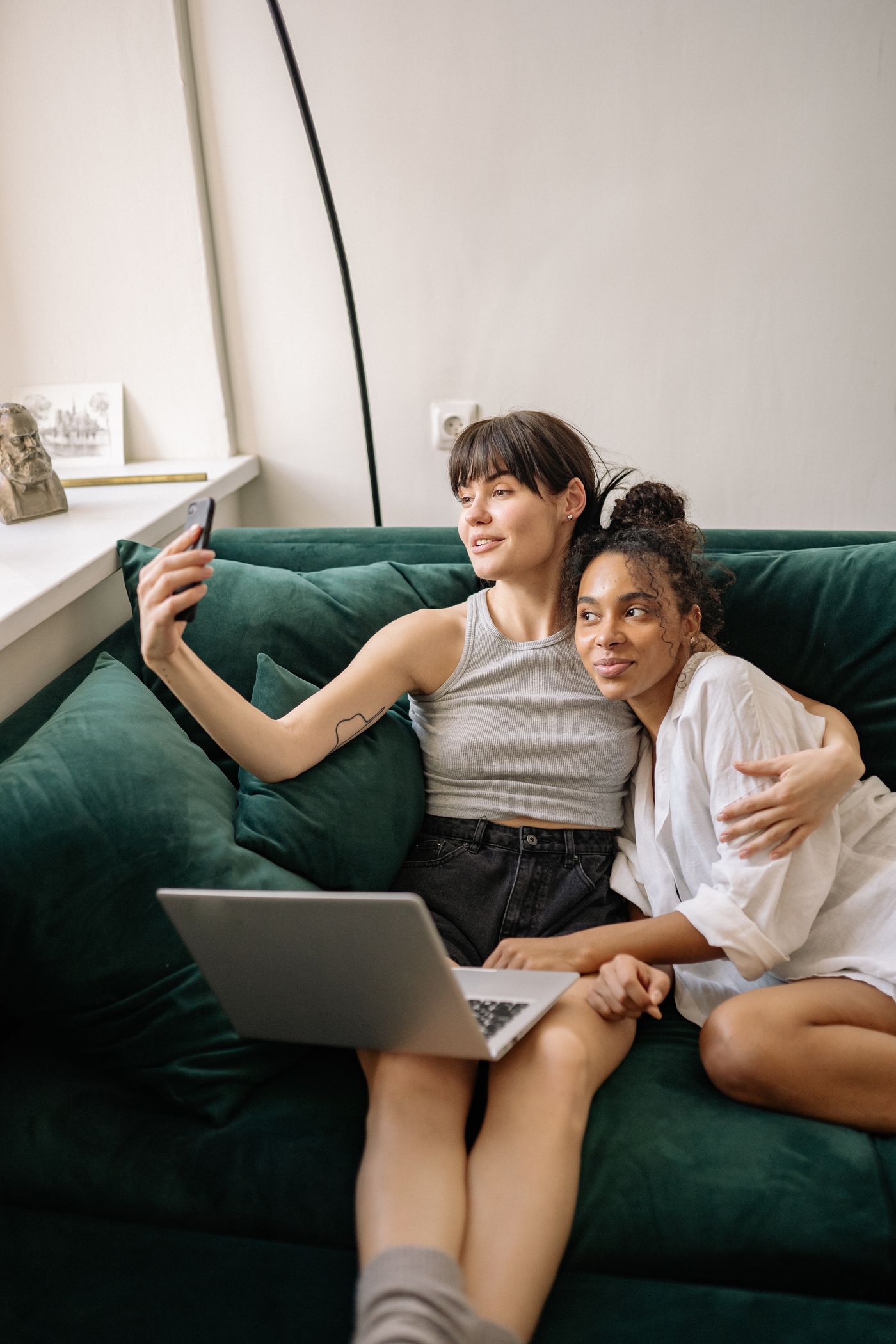 Two adult women sitting close together on a green sofa with a laptop