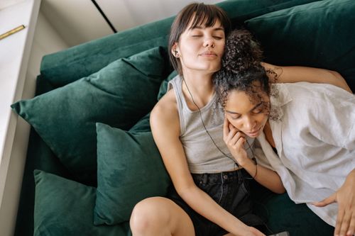 Free Interracial lesbian couple enjoying music together on a cozy couch. Stock Photo