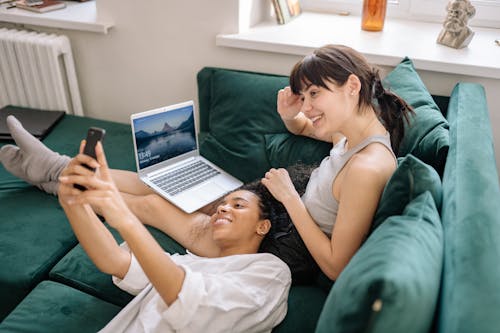 Women Using a Laptop and a Phone While on the Couch