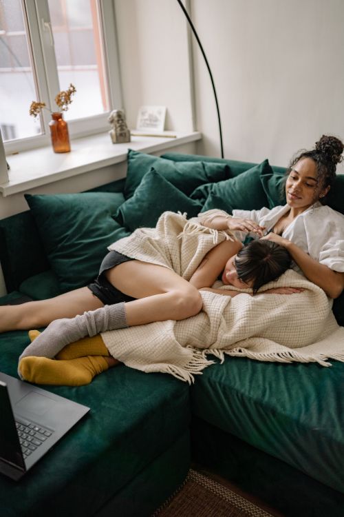 Free A diverse couple cuddling under a blanket on a sofa in a cozy living room setting. Stock Photo
