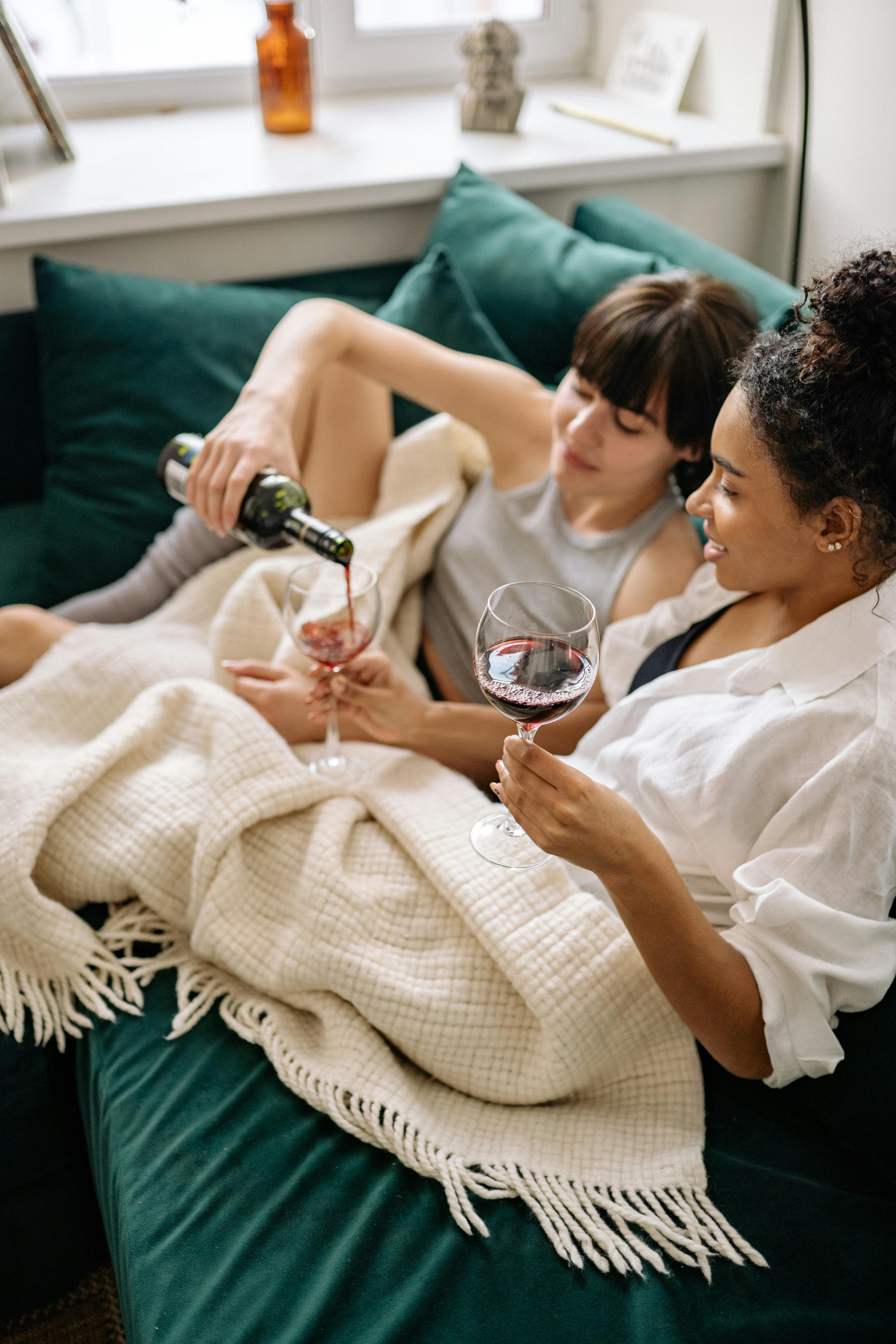 Two women in cozy setting with wine, showcasing intimacy and relaxation.