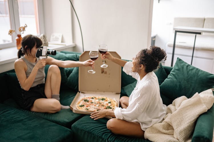 Women Drinking Wine And Eating Pizza On The Couch