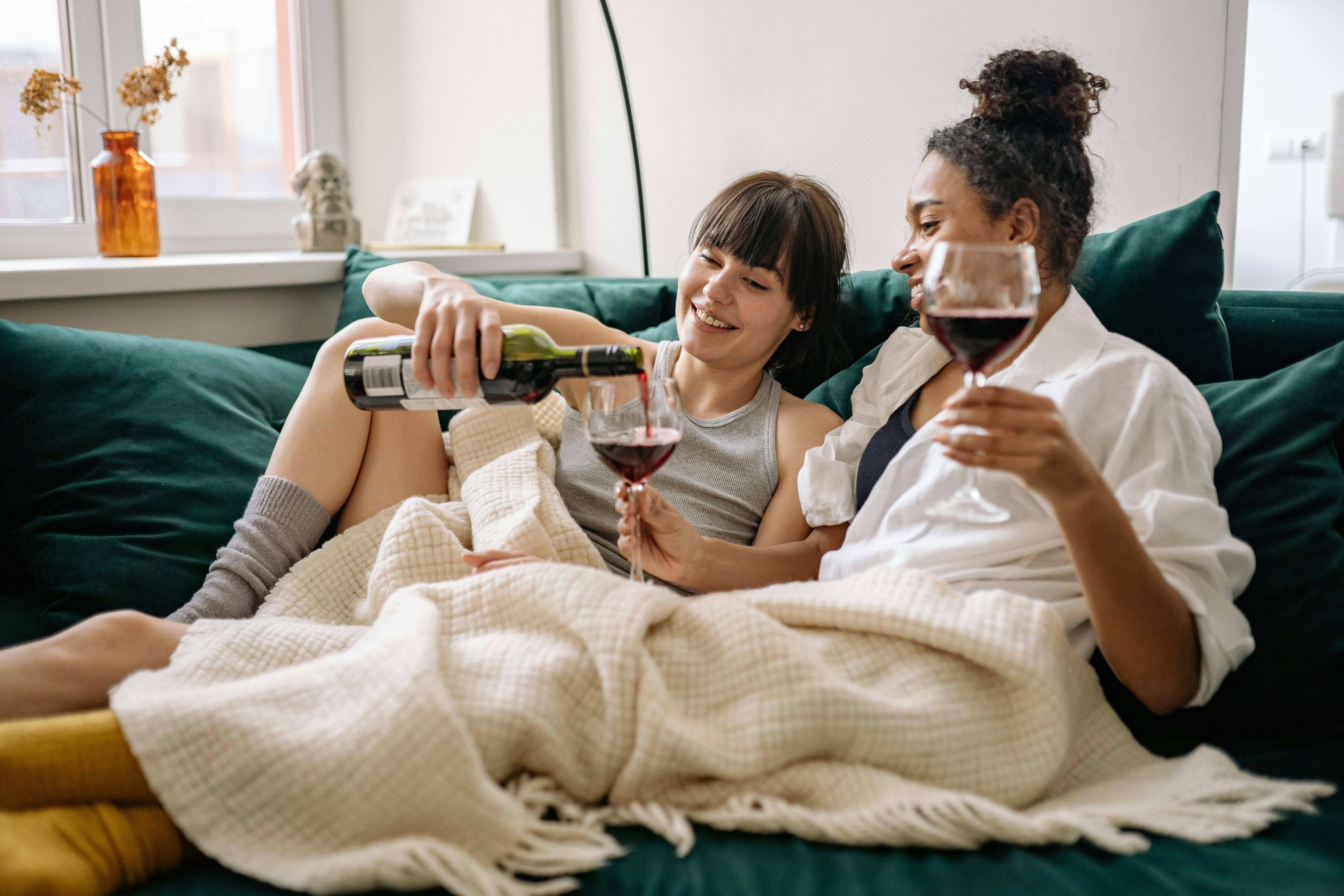 Lesbian couple enjoying red wine together indoors, exuding warmth and love.