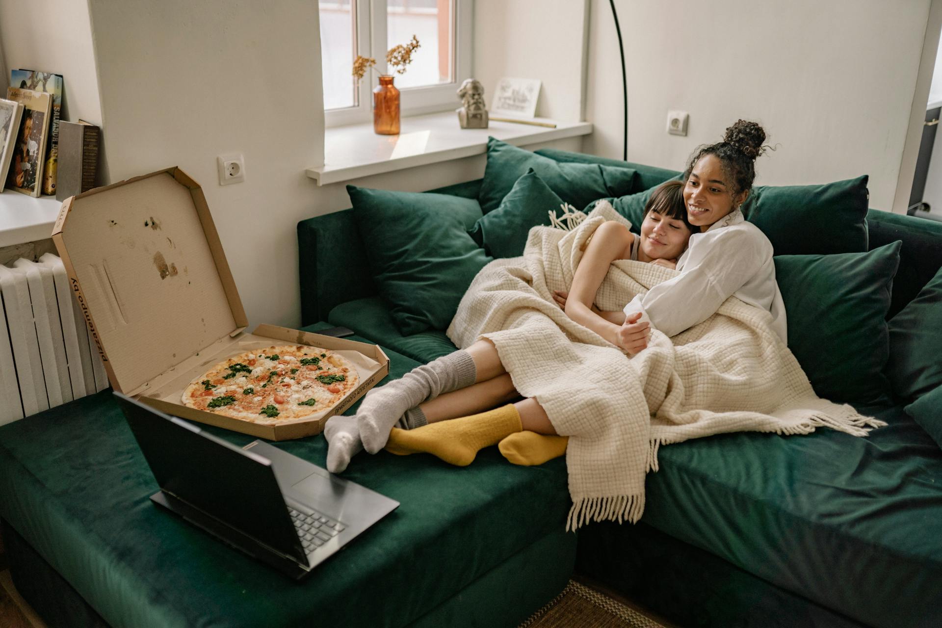 Lesbian couple cuddles on the couch while enjoying a pizza and relaxation at home.