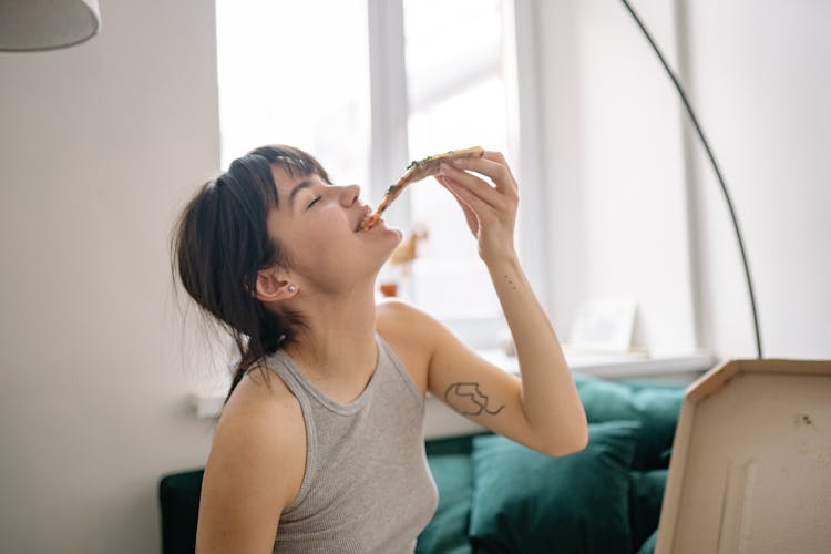 A Young Woman In Gray Tank Top Enjoying Eating Pizza