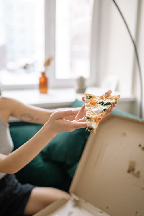 Free A person holding a slice of pizza in a cozy living room setting, next to an open pizza box. Stock Photo
