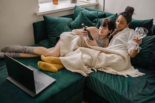 Free Lesbian couple relaxing at home, enjoying wine and watching a movie on the couch. Stock Photo