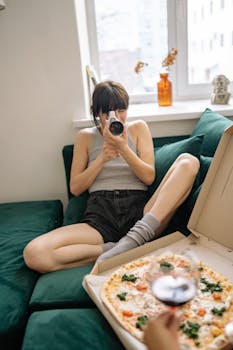 Cozy home scene with woman recording on a camcorder near a pizza box.