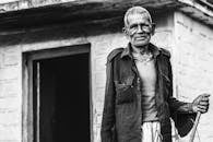 一位年长的印度男子面带微笑，站在村庄房屋前的黑白肖像中