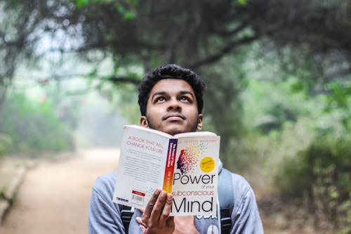 Free Man in Grey Shirt Holding Opened Book Looking Upward Stock Photo