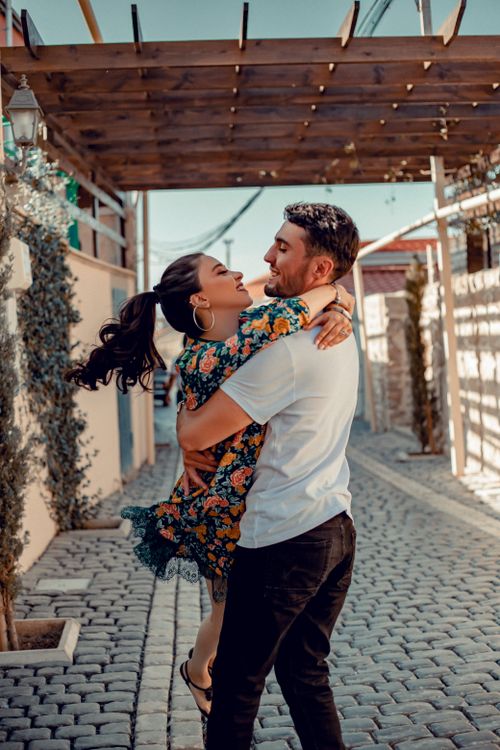 Free Side view of cheerful boyfriend lifting positive girlfriend in dress while standing on paved street in city during romantic date Stock Photo