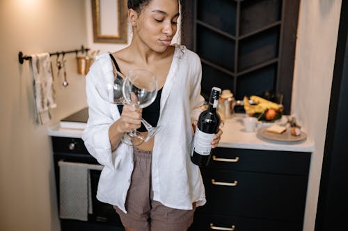 Photo of a Woman Holding a Bottle of Wine and Wine Glasses