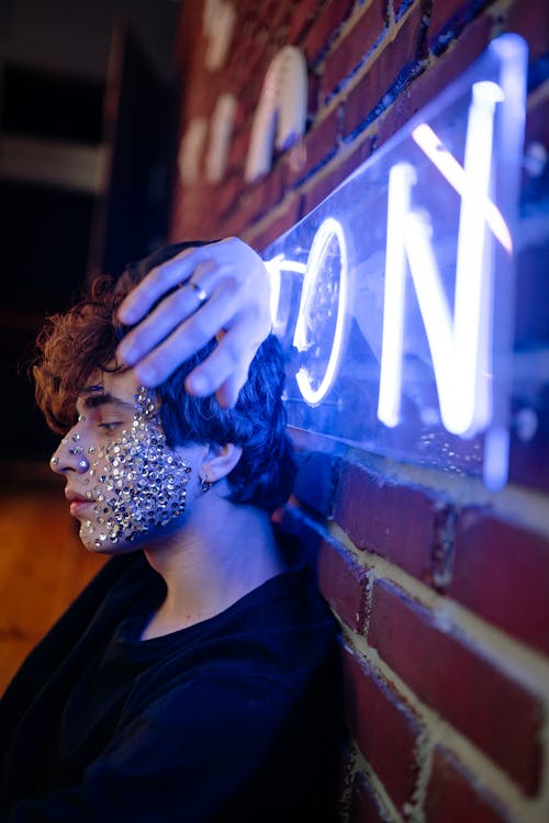 A Young Person with Silver Sequin on Cheek Leaning on a Wall with Singnage