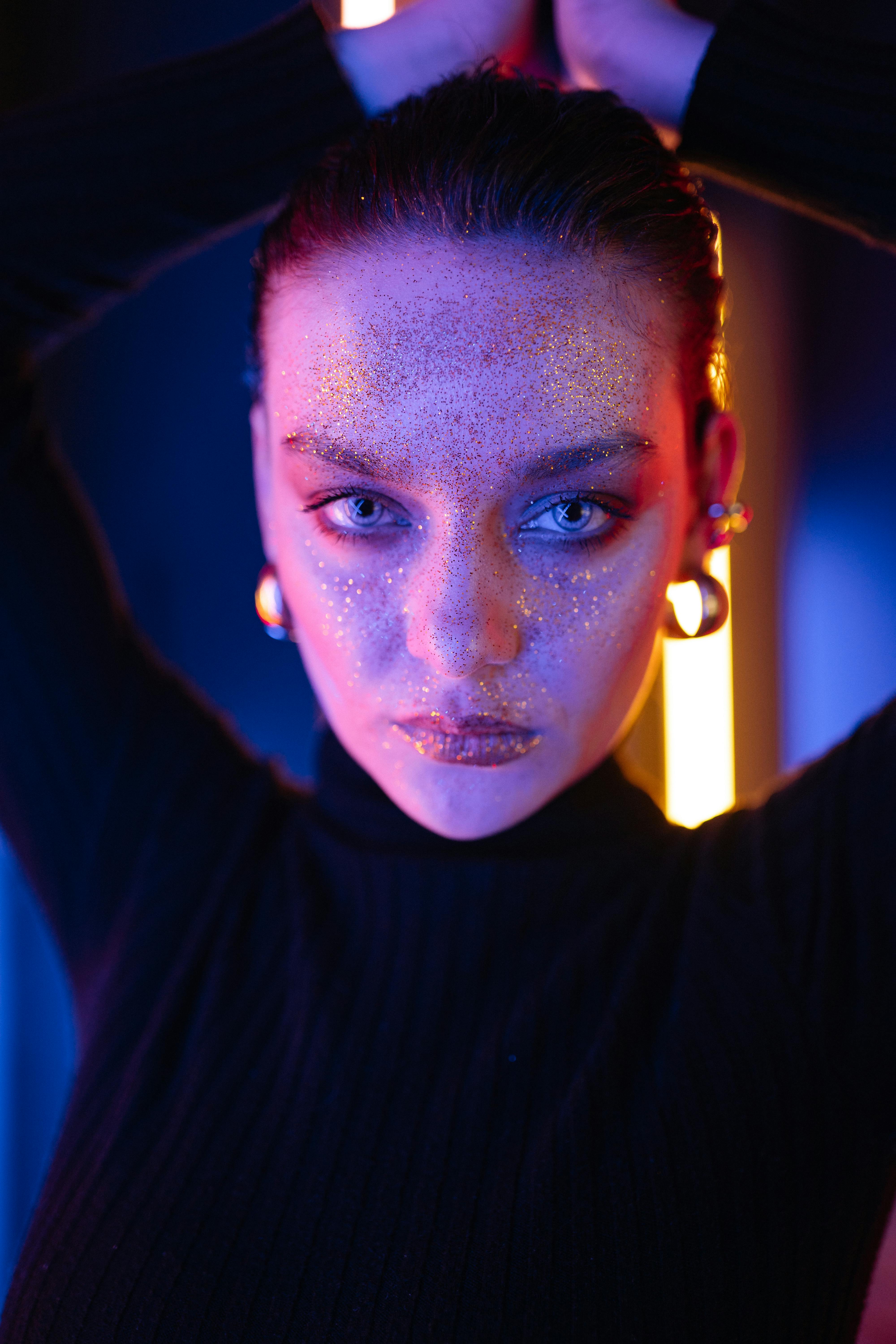 Striking portrait of a woman with glitter makeup in dramatic lighting, capturing artistic expression.