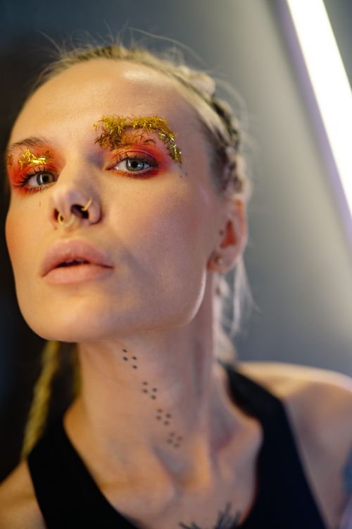 Free Close-up of a woman with creative makeup, nose piercing, and tattoos, exuding unique style. Stock Photo