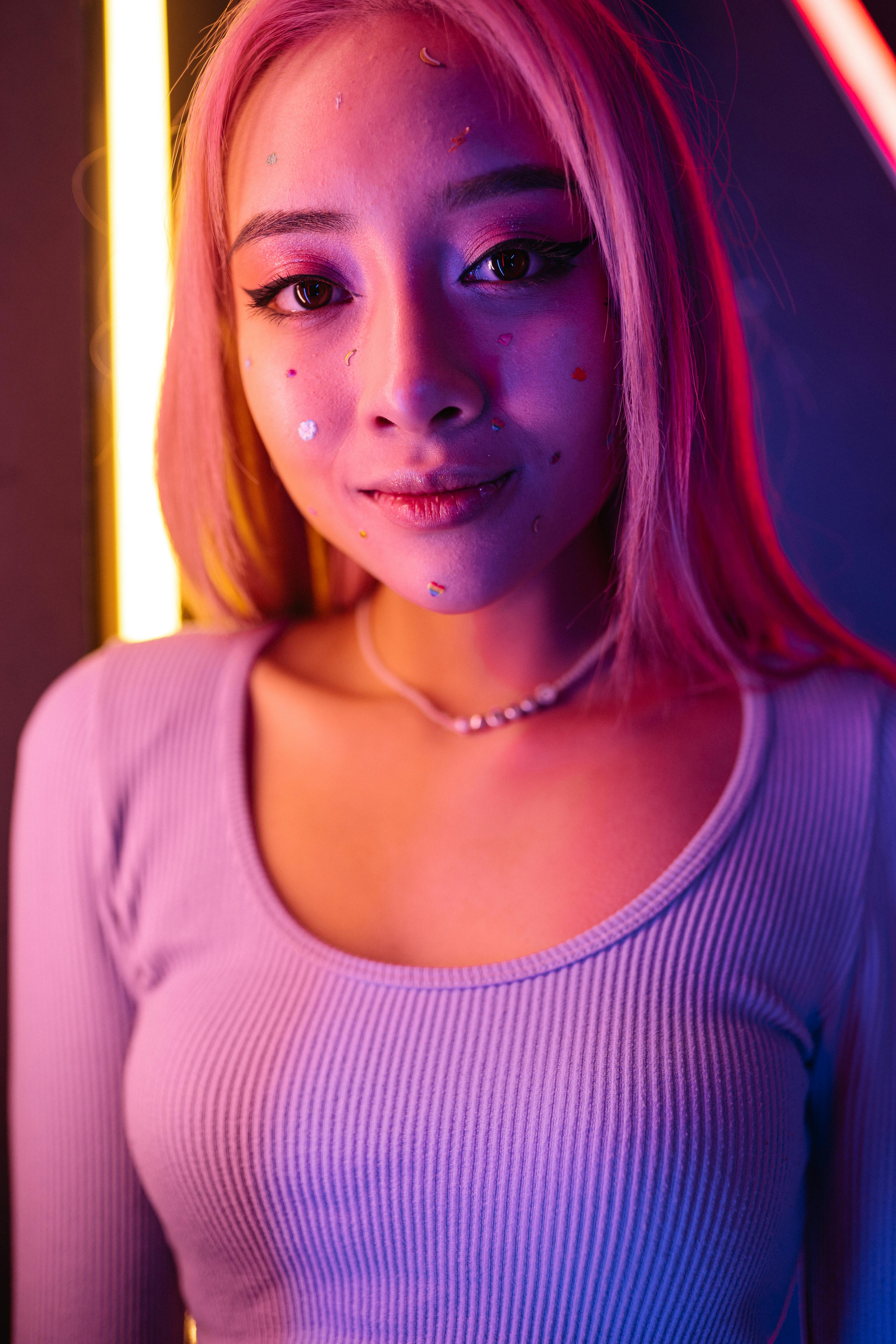 A young woman with glowing neon lights and colorful stickers on her face smiles confidently.