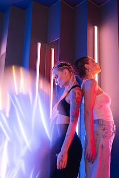 Two women back to back with neon glow in artistic portrait, showcasing creative makeup.