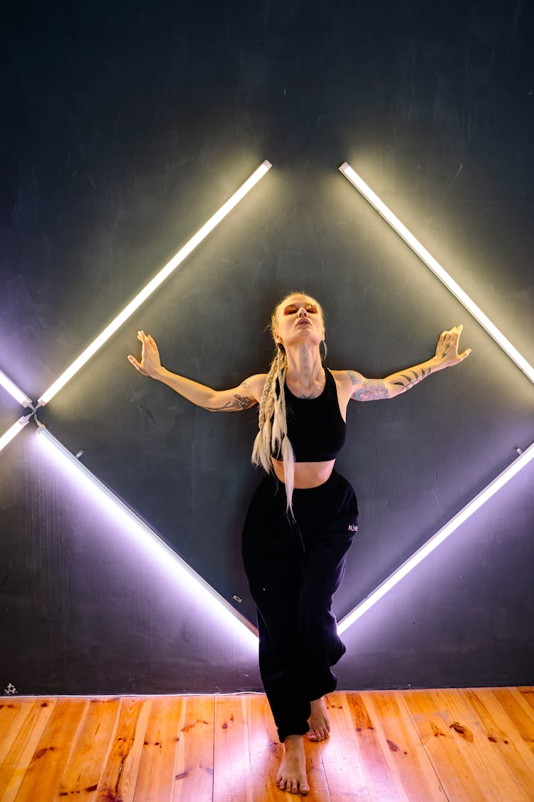 Woman Wearing Black Crop Top And Pants Leaning On Wall With Lights