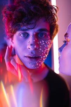Close-up of a person with creative makeup and neon lighting, featuring artistic sequins and a vibrant expression.