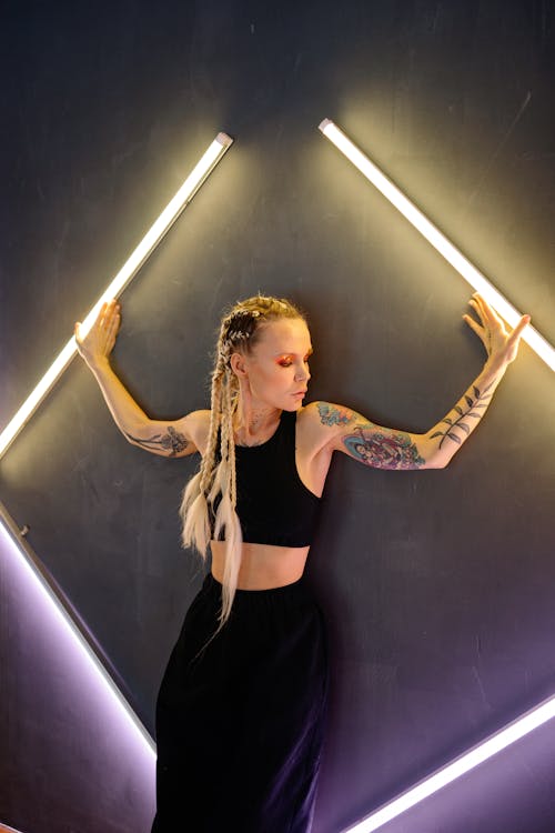 A Woman with Arm Tattoo Leaning and Posing on Wall with Lights