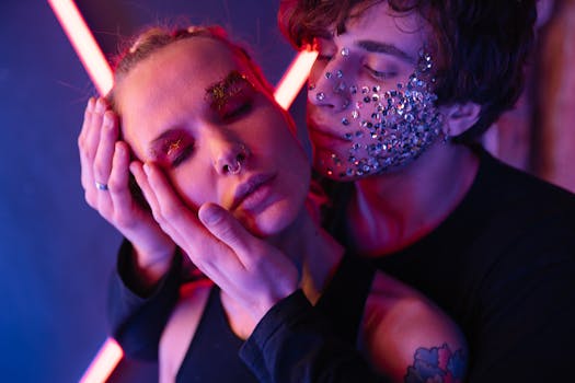 Creative portrait of two young people embracing, adorned with glitter and artistic makeup under vibrant neon lights.
