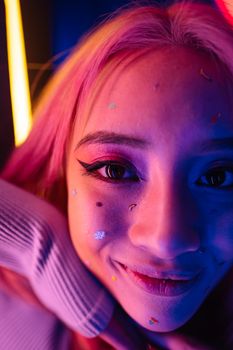 Close-up of a smiling young woman with pink hair and colorful stickers on her face.