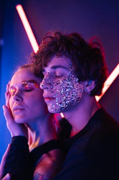 Artistic close-up of a couple with creative makeup and neon lights, emphasizing sequins and colors.