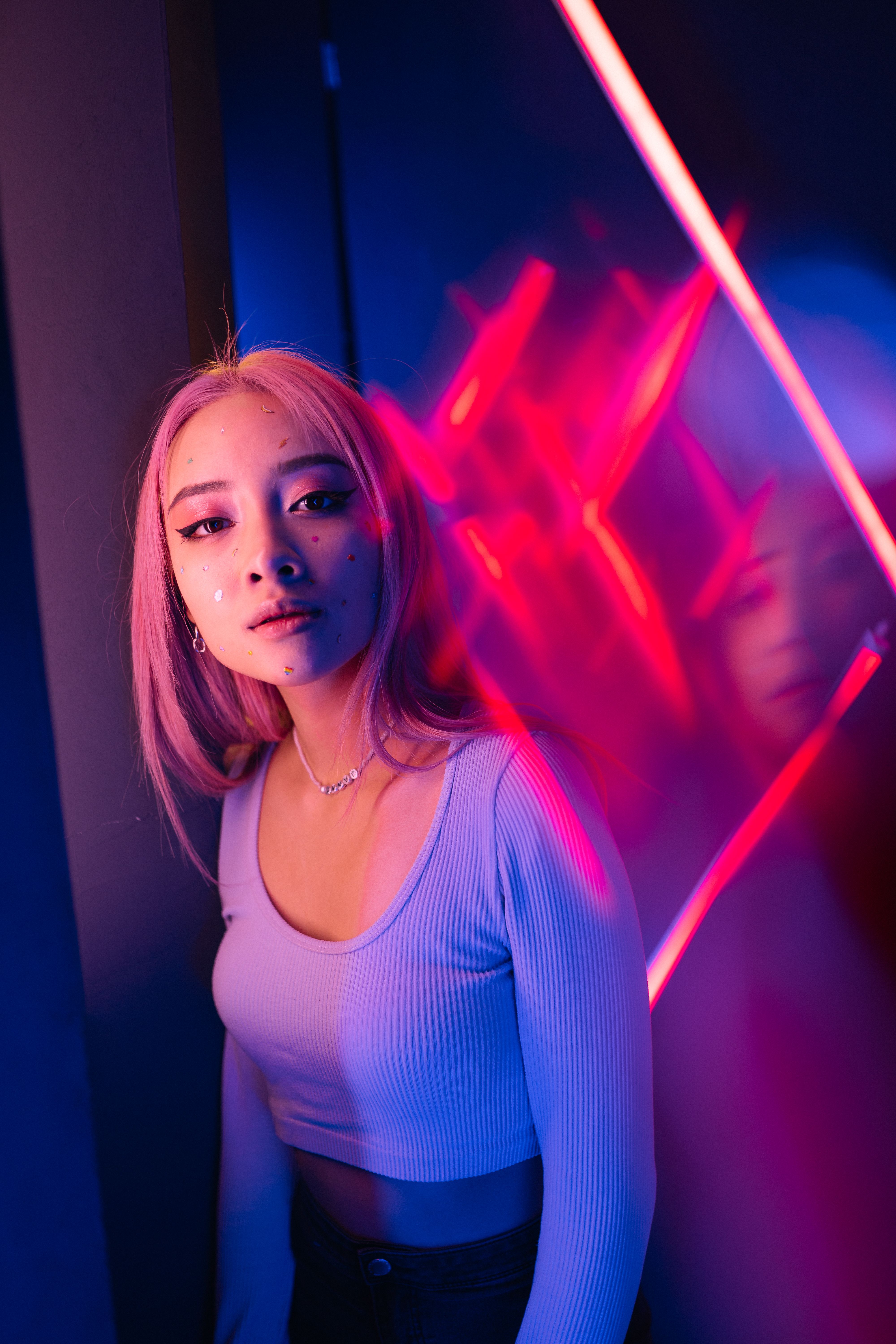 Young woman with pink hair posing in neon lights, creating a modern and stylish conceptual look.