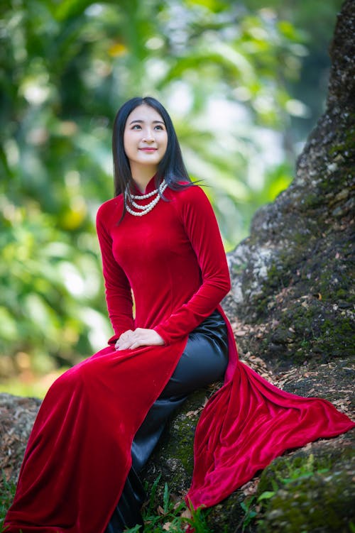 Charming Asian woman sitting in red dress in forest