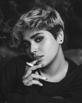 Artistic black and white portrait of a woman smoking and looking at the camera.