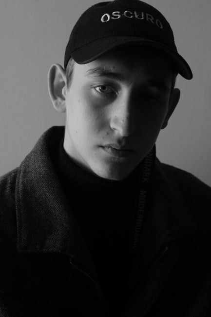 Black and white portrait of a young man wearing a cap with a serious expression.