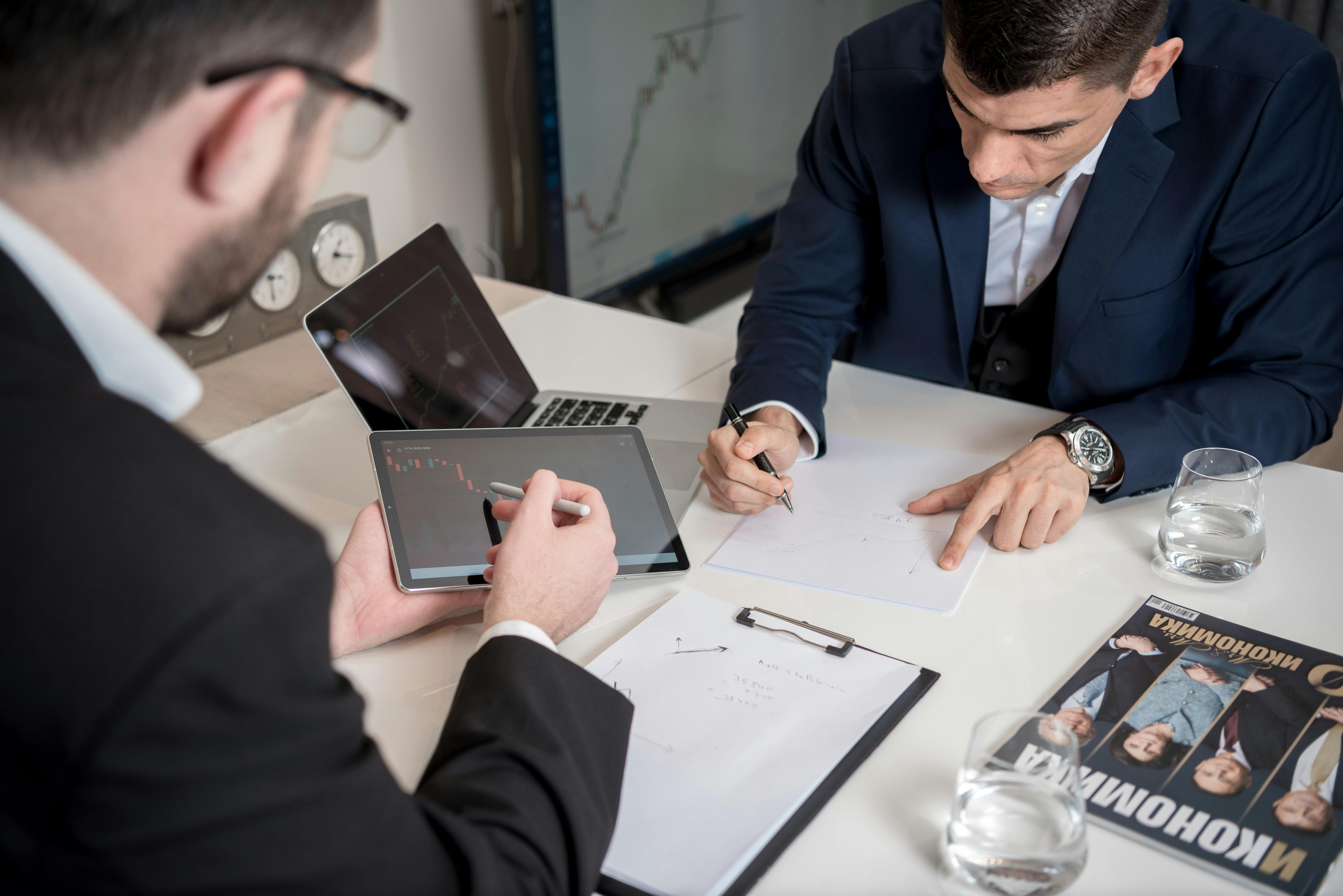 man in black suit jacket holding a tablet pointing on a graph