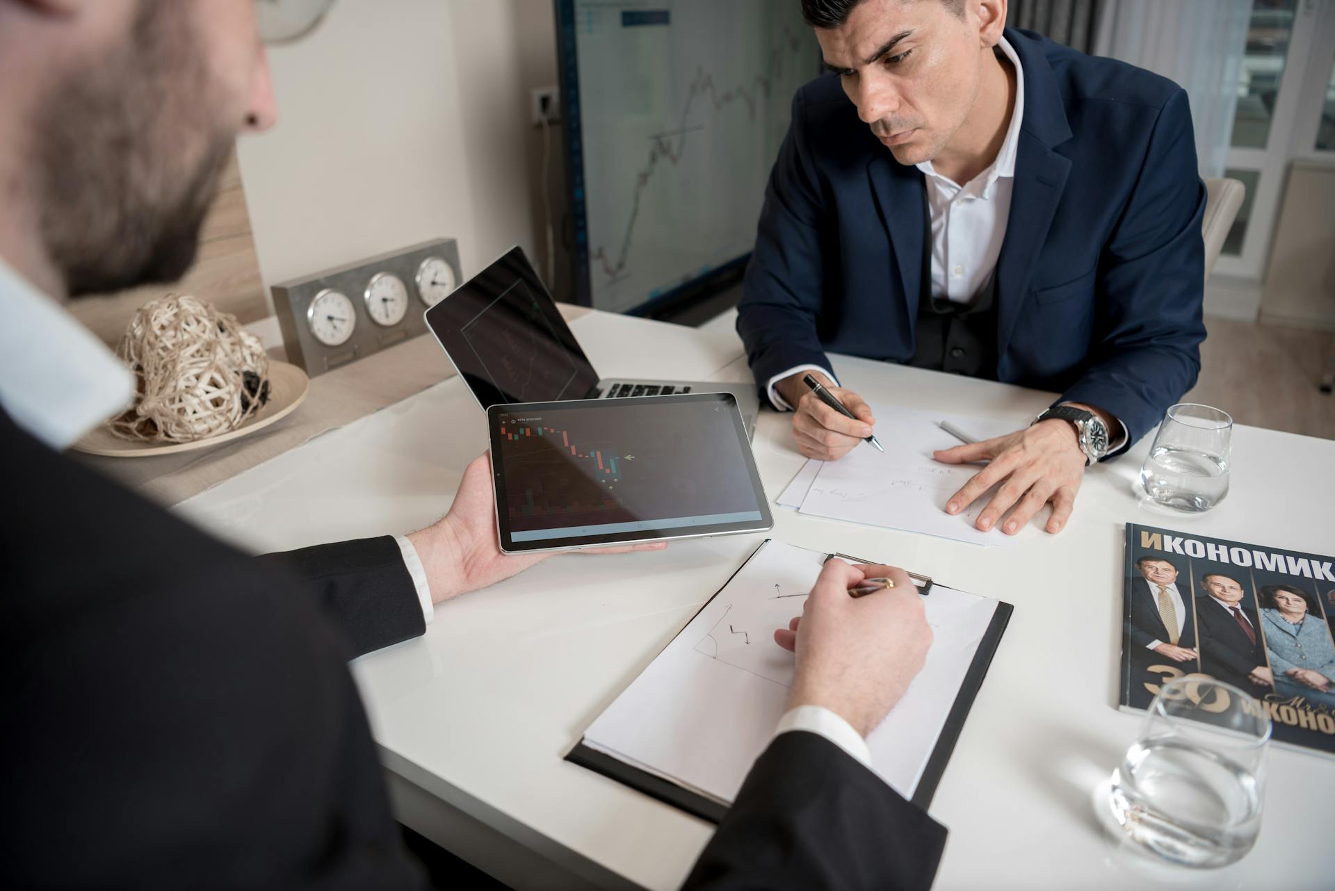 Business professionals discussing market data using a digital tablet and documents in a modern office setting.