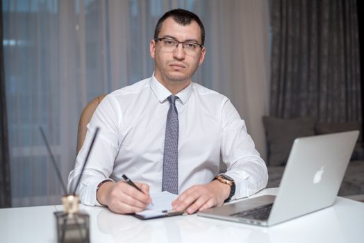 Professional man in corporate attire sitting at desk with laptop, engaged in work.