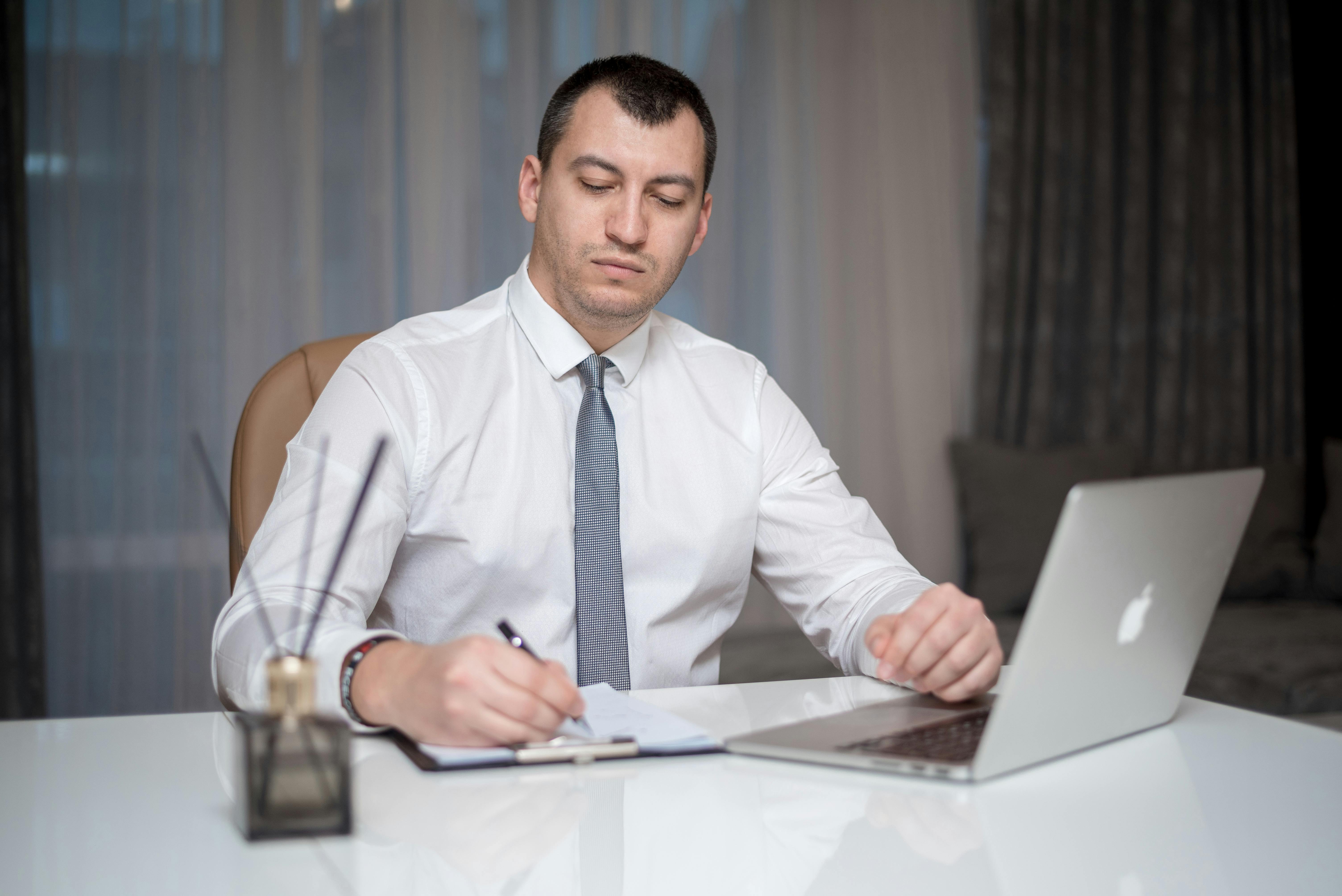 Business professional in a white shirt and tie reviewing documents with a laptop, symbolizing careful evaluation of short-term loan terms before signing