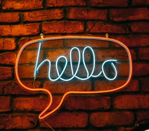 Free Bright neon 'hello' sign in speech bubble shape against a rustic brick wall. Stock Photo