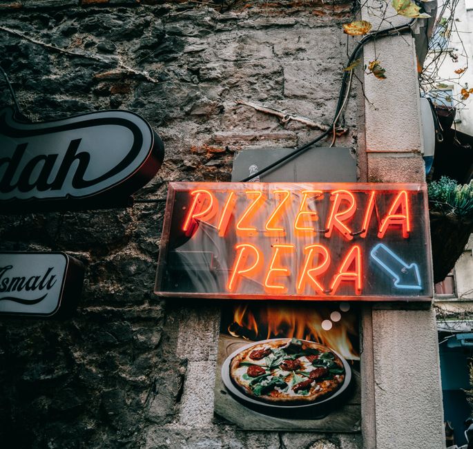 Vibrant neon 'Pizzeria Pera' sign glowing on an Istanbul street wall.