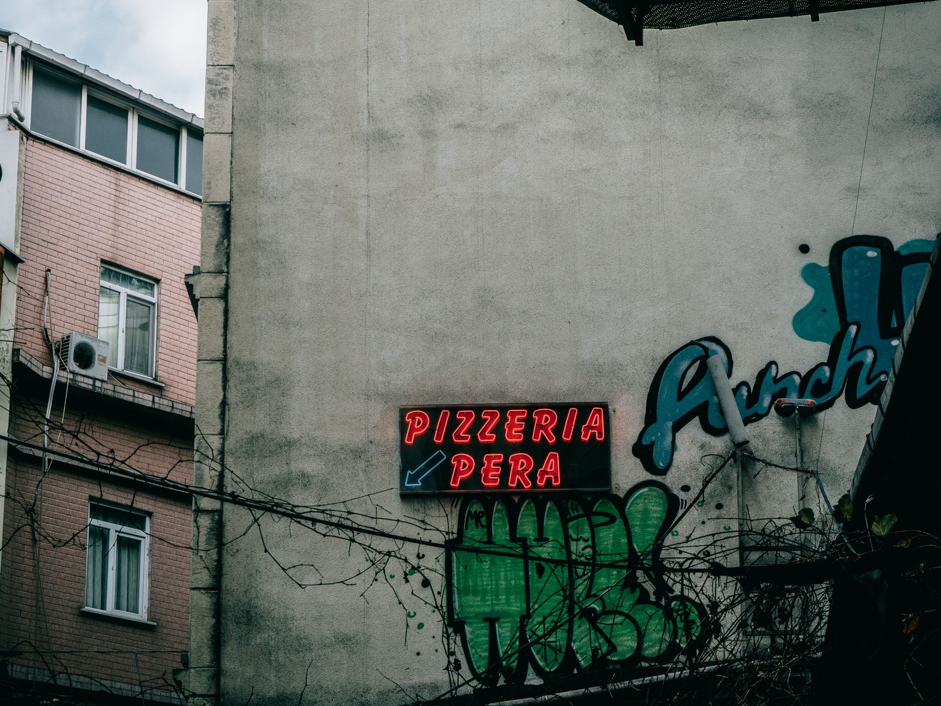 A vibrant neon sign for Pizzeria Pera on a graffiti-decorated wall in Istanbul.