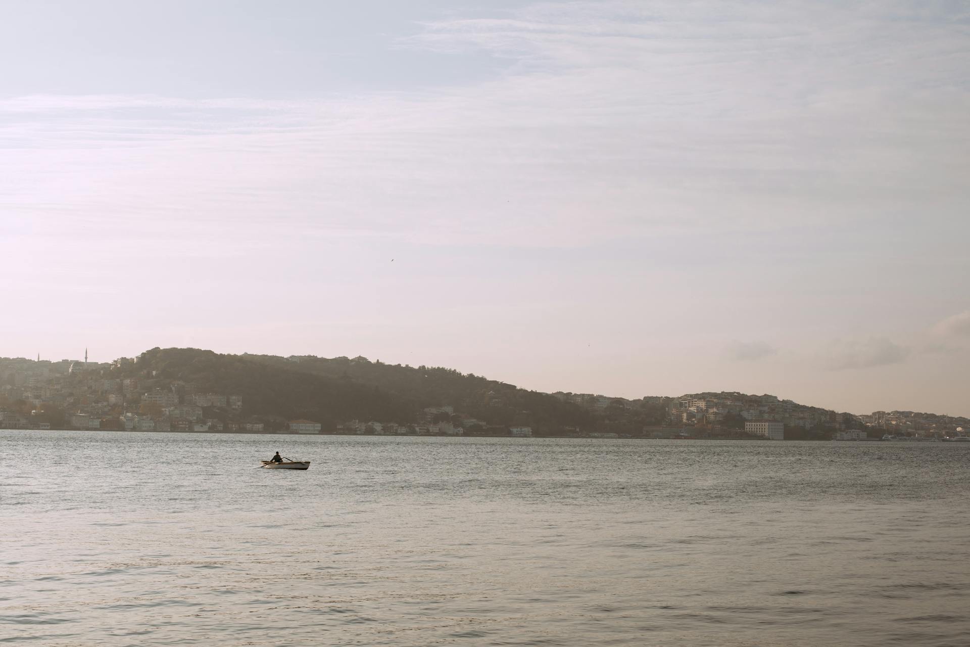 Tranquil scene of a lone boat on the Bosphorus with an Istanbul cityscape in the background.