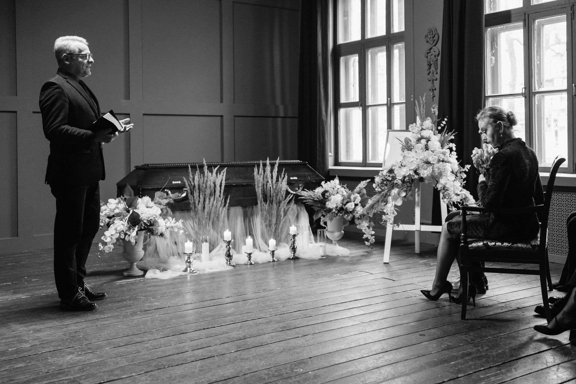 A somber funeral scene in grayscale showing a pastor and woman mourning.