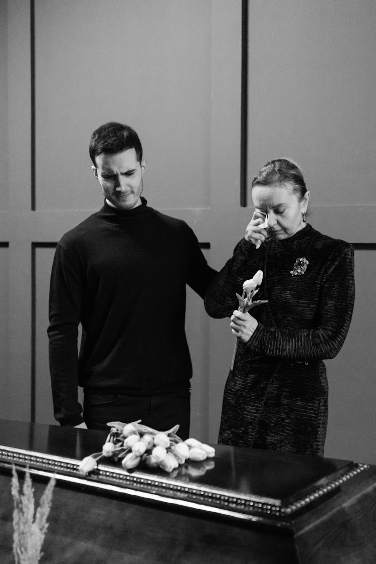 A Young Man And An Elderly Woman Crying In Front Of A Coffin