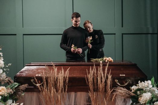 An Elderly Woman Leaning on a Man's Shoulder Near a Wooden Coffin