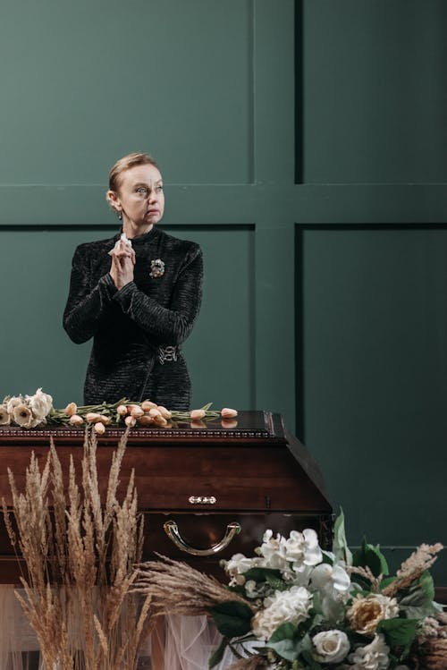 Woman in Black Coat Standing Beside the Coffin